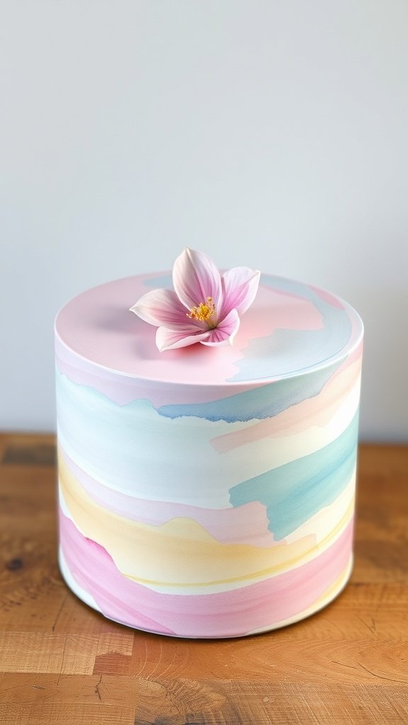 A round cake with a watercolor design in soft pastel colors and a flower on top.