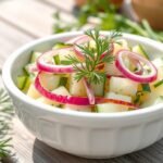 A bowl of cucumber salad with vinegar garnished with fresh herbs on an outdoor table setting