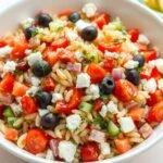 Mediterranean orzo pasta salad with colorful vegetables, feta cheese, and herbs in a white bowl