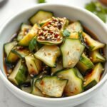 Smashed cucumber salad in a white bowl with sesame seeds and cilantro garnish