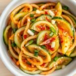 Spicy cucumber salad in a white bowl garnished with sesame seeds and red pepper flakes