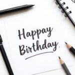 Various art supplies for creating happy birthday doodles including pens, markers, and paper